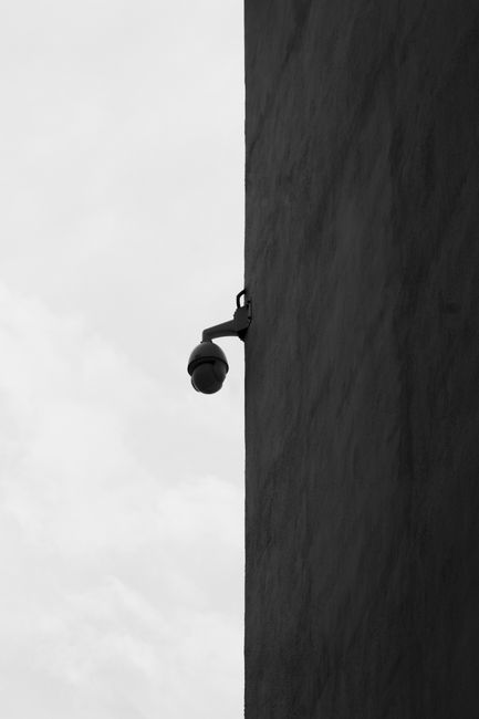 Black and white image of a CCTV camera mounted on a building corner.