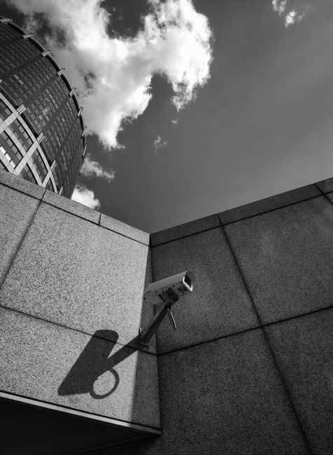 Low angle shot of a building facade with security camera against a cloudy sky.